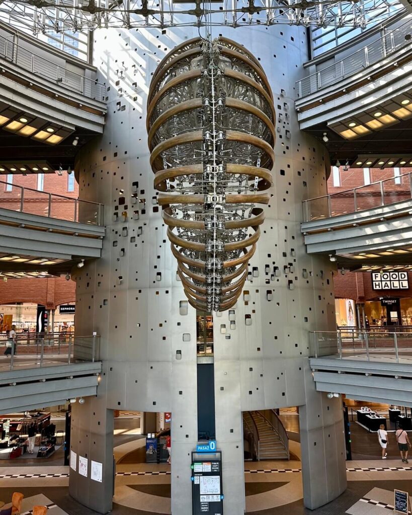 Large modern sculpture resembling a ribcage hangs in the center of a shopping mall atrium.