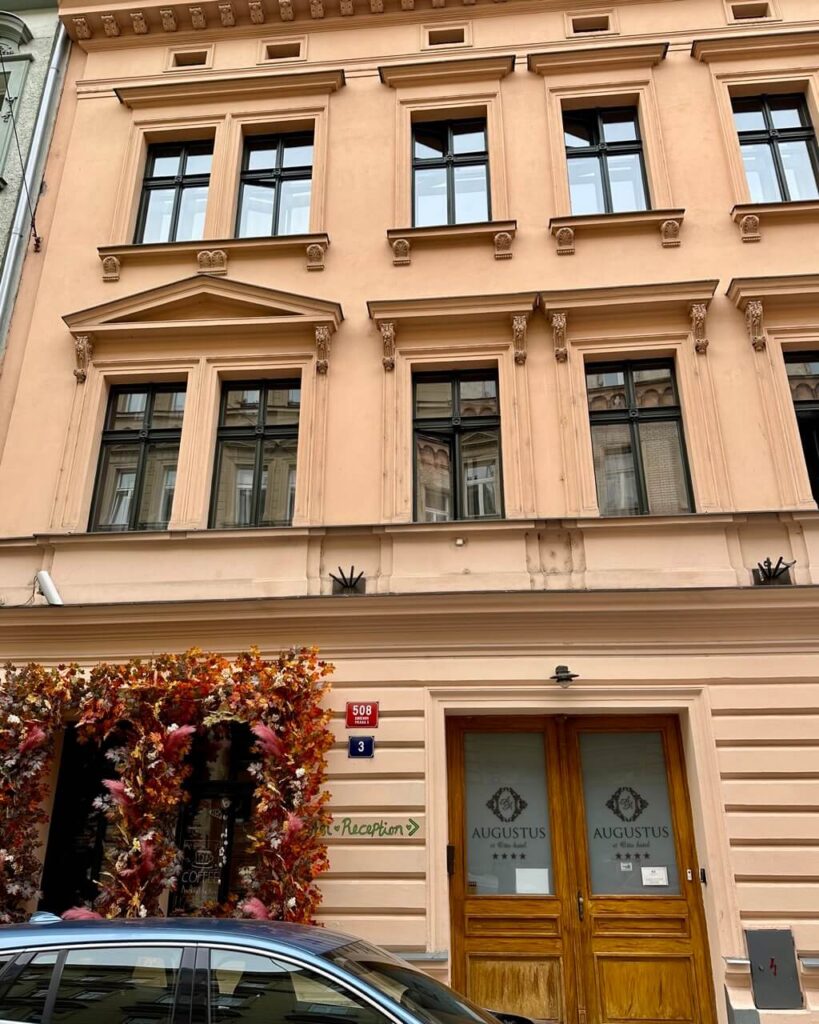 Augustus Prague hotel entrance with cream colored historic facade and wooden double doors in a central Prague neighborhood.