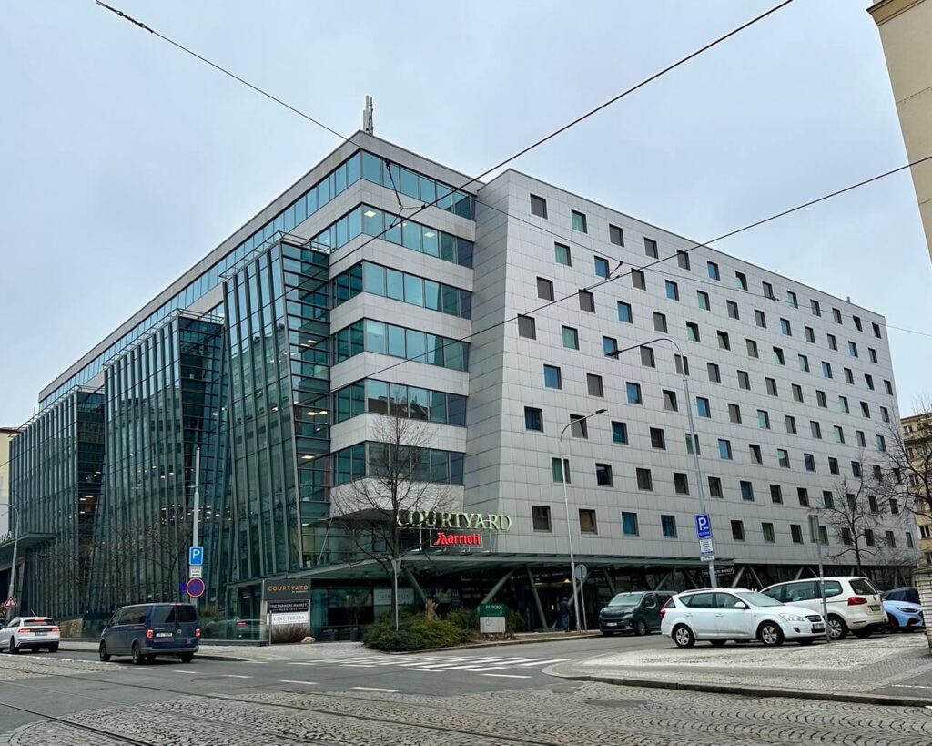 Courtyard Prague hotel by Marriott with glass corner facade on a busy city street in a business district Prague neighborhood.