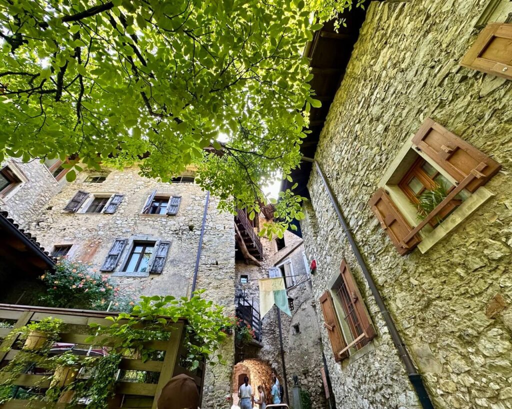 Stone houses in Canale di Tenno rise around a narrow courtyard under bright green leaves and wooden shutters.
