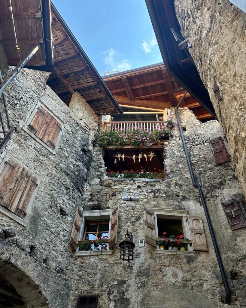 Historic stone courtyard in Canale di Tenno with wooden shutters. Flower boxes. Hanging cloth. And leafy branches overhead.