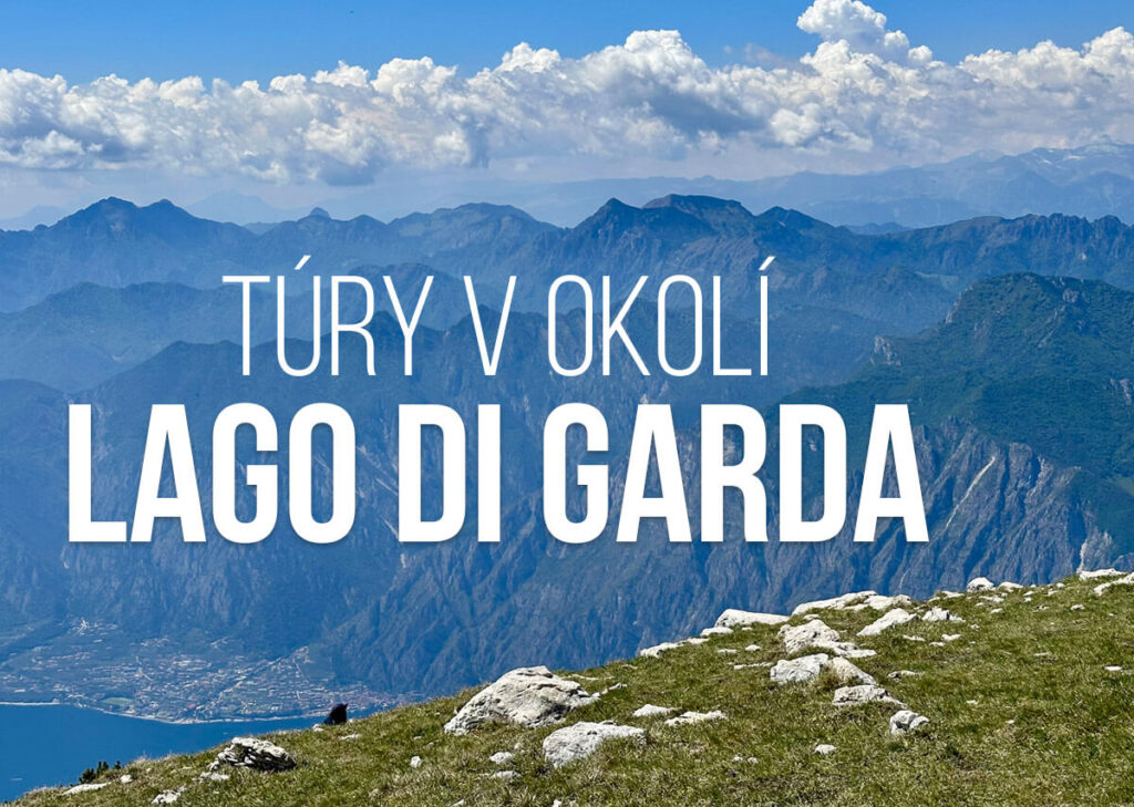Panoramatický výhled z turistické trasy u Lago di Garda s kamenitou zelenou loukou nad jezerem a vrstvenými modrými horami pod jasnou oblohou plnou bílých mraků. Text říká „TÚRY V OKOLÍ LAGO DI GARDA“.