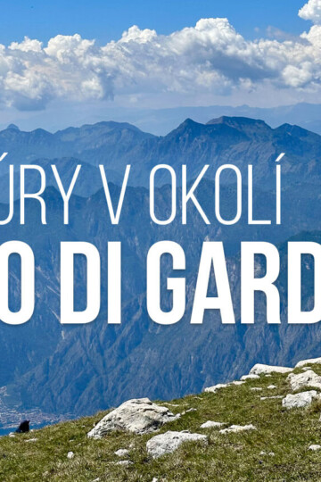 Panoramatický výhled z turistické trasy u Lago di Garda s kamenitou zelenou loukou nad jezerem a vrstvenými modrými horami pod jasnou oblohou plnou bílých mraků. Text říká „TÚRY V OKOLÍ LAGO DI GARDA“.