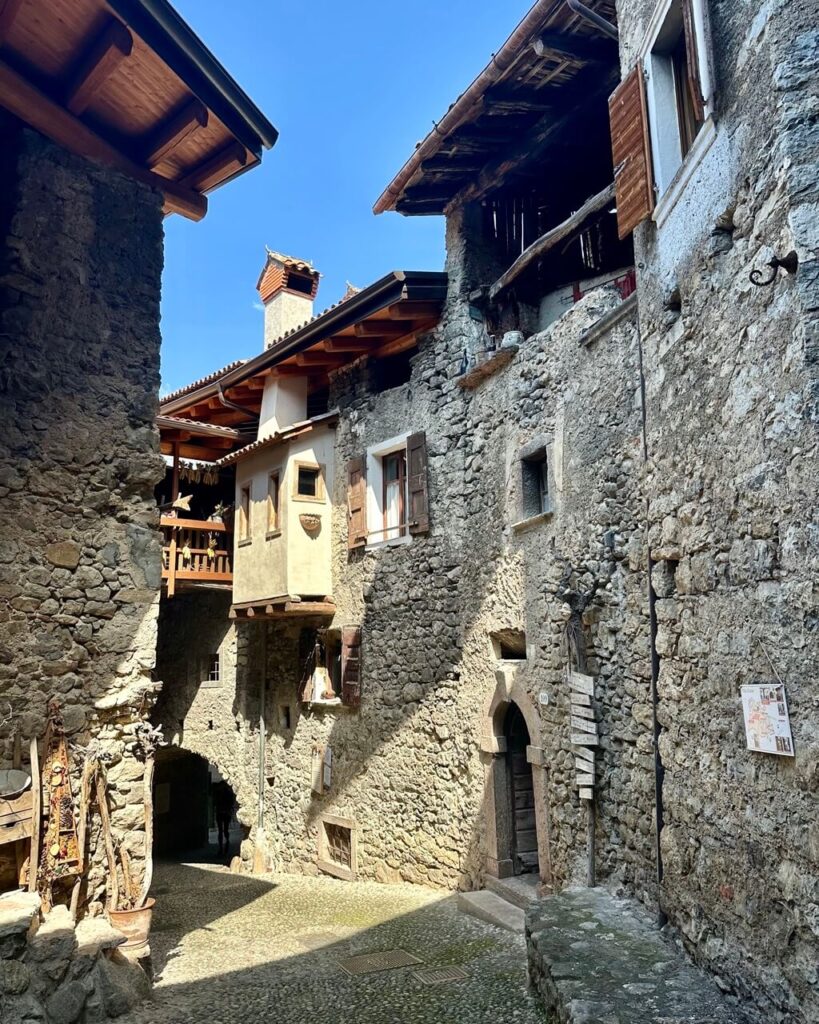 Sunlit stone lane in Canale di Tenno with rough walls. Wooden balconies. Shutters. And a narrow cobblestone passage.